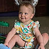 animal_ears, baby, blue_eyes, carpet, casual, child, colorful_clothing, cute, happy, headband, indoor, infant, person, playful, portrait, sitting, smile, socks, toddler, toy
