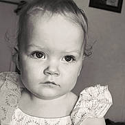 Skyler joined the competition — help win amazing prizes! child, toddler, portrait, black_and_white, curly_hair, dress, patterned_clothing, indoor, close_up, serious_expression, face, young_child, person, baby, cute, head_and_shoulders, monochrome, soft_light, wall_art, photography
