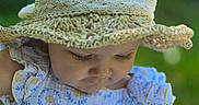 Skyler is registered to the contest to win money with this photo: baby, child, hat, crocheted_hat, dress, blue_dress, floral_pattern, outdoor, nature, green_background, portrait, closeup, infant, cute, sun_hat, summer, soft_light, face, person, young_child