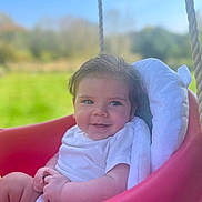 Kaden is registered to the contest to win money with this photo: baby, smile, swing, outdoor, child, white_clothing, blanket, red_swing, grass, blue_sky, happy, infant, nature, sunny, portrait, person, seat, rope, cute, young