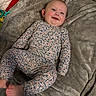 baby, child, smiling, face, blue_eyes, floral_outfit, blanket, soft_texture, lying_down, cute, infant, happy, indoors, skin, feet, head, ears, person, comfort, warm