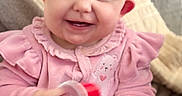 Lorelai is registered to the contest to win money with this photo: baby, smiling, pink_clothing, headband, bow, toy, indoor, couch, blanket, happy, child, face, cute, infant, portrait, hand, sitting, cozy, soft_texture, home