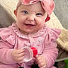 baby, smiling, pink_clothing, headband, bow, toy, indoor, couch, blanket, happy, child, face, cute, infant, portrait, hand, sitting, cozy, soft_texture, home
