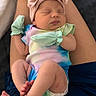 newborn, baby, infant, sleeping, headband, bow, mittens, onesie, tie_dye, colorful, legs, feet, toes, person, lap, skin, close_up, soft_lighting, peaceful, resting