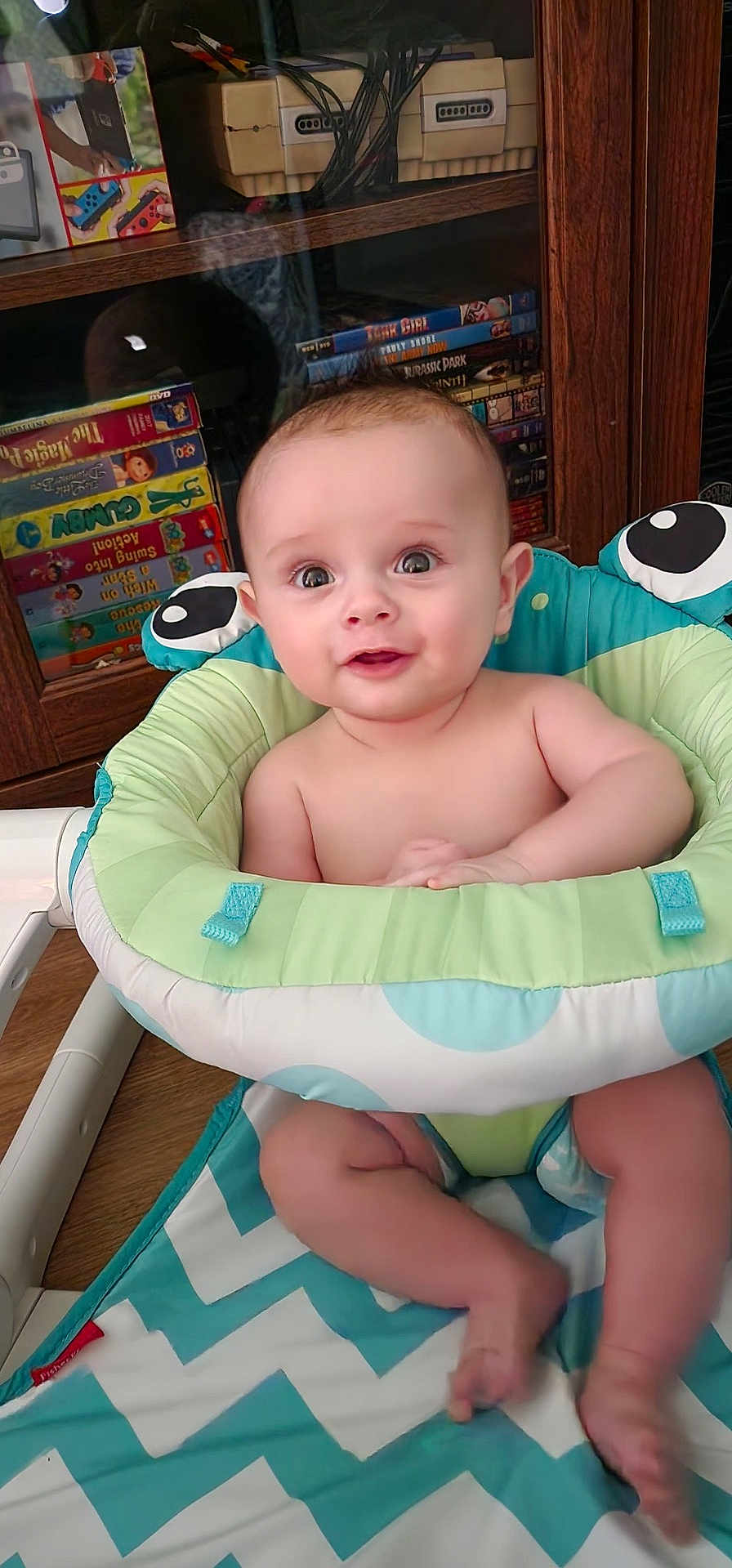 Harvey joined the competition — help win amazing prizes! baby, child, infant, baby_seat, happy, smiling, indoor, wooden_cabinet, video_games, retro, console, toys, furniture, floor, colorful, person, cute, feet, arms, face
