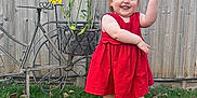 Amelie joined the competition — help win amazing prizes! toddler, child, red_dress, grass, flower_pot, flowers, metal_bicycle, fence, outdoor, smiling, playful, greenery, yard, plant, person, footwear, socks, happy, garden, summer