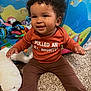 Everleigh is registered to the contest to win money with this photo: toddler, child, smiling, curly_hair, indoor, carpet, plush_toy, white_bear, colorful_toys, long_pants, rust_shirt, text_on_clothing, play_area, underwater_theme, fish_pattern, happy, cute, sitting, person, earring