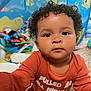 baby, child, curly_hair, indoor, colorful, toys, play_area, carpet, face, person, clothing, long_sleeve, expressionless, closeup, young_child, cute, portrait, toddler, room, background