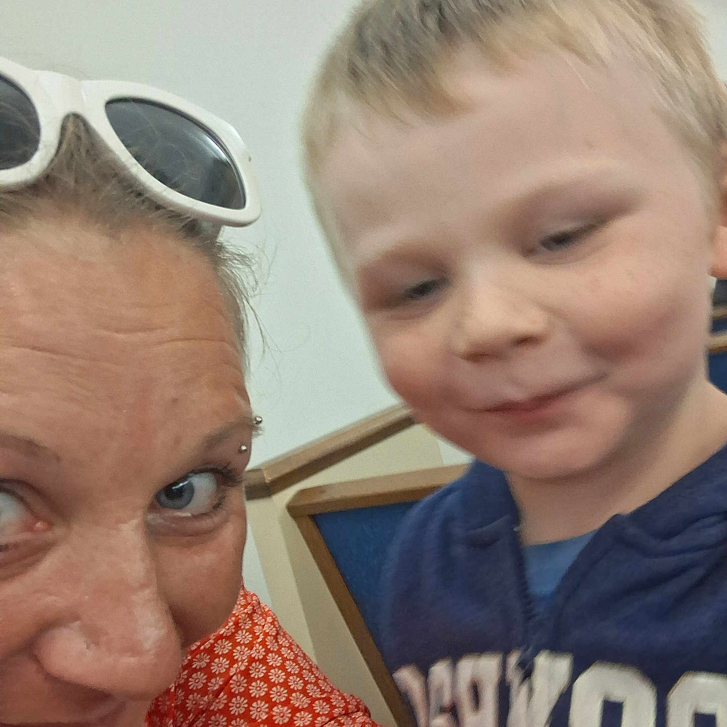 River Lewis is registered to the contest to win money with this photo: woman, child, selfie, face, person, indoors, blue_hoodie, sunglasses, smile, closeup, casual, portrait, seated, chair, wall, hair, skin, clothing, people, eyebrows