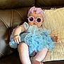 accessory, baby, blue_tutu, brown_leather, child, couch, cute, face, fashion, floral_onesie, foot, hand, headband, indoor, infant, person, pillow, portrait, sitting, sunglasses
