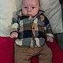 baby, infant, child, plaid_shirt, brown_pants, gray_socks, pillow, blanket, red_blanket, indoor, person, face, head, eyes, small_hands, seated, cozy, cute, casual_clothing, portrait