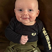 Maverick joined the competition — help win amazing prizes! baby, smiling, face, child, clothing, black_shirt, olive_pants, sitting, fist, happy, portrait, indoor, infant, cute, young_child, person, front_view, bright_eyes, human, casual_wear
