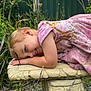 Elliana is registered to the contest to win money with this photo: bench, child, close_up, daytime, earring, fence, garden, girl, grass, happy, lying_down, nature, outdoor, pigtail, pink_dress, plants, playful, portrait, smile, stone_bench