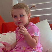 Elliana is registered to the contest to win money with this photo: blinds, child, couch, cute, eating, expression, face_filter, girl, hearts, home_interior, indoor, orange_couch, pigtails, pillow, pink_dress, playful, portrait, sitting, snack, toddler