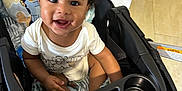 Aiden is registered to the contest to win money with this photo: toddler, child, smiling, curly_hair, stroller, indoor, baby_clothes, seat, happy, person, cute, playful, cushion, toy_pattern, black_hair, skin, infant, young_child, sitting, bright