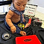 Aiden joined the competition — help win amazing prizes! baby, child, toddler, tools, hammer, drill, tape_measure, bandana, black_blanket, floor, sign, indoor, curly_hair, skin, foot, hand, red_toolbox, mechanic, playing, sitting
