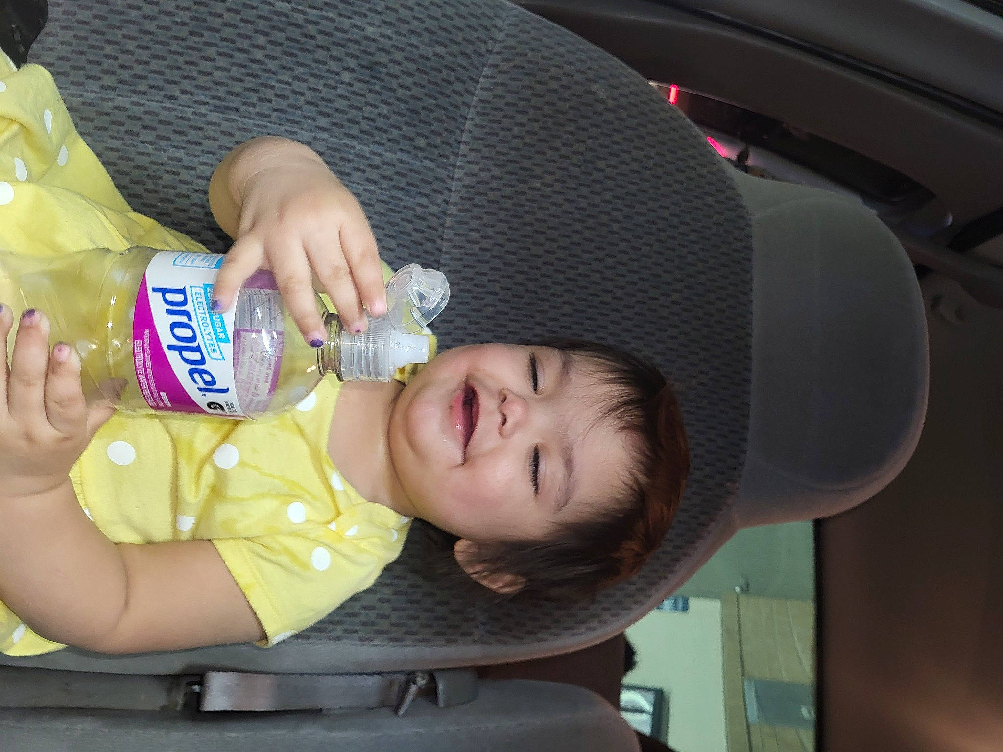 Kailani is registered to the contest to win money with this photo: baby, baby_bottle, bottle, cheek, child, drinking_water, drinkware, finger, hand, hat, joy, mouth, nail, person, plastic_bottle, skin, smile, sun_hat, toddler, vehicle_door