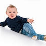 baby, child, blue_eyes, curly_hair, navy_sweater, blue_jeans, socks, smiling, playful, reclining, white_background, studio_photo, happy, cute, small_hands, infant, portrait, casual_clothing, one_person, indoor