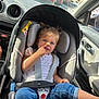 car_interior, car_seat, child, daytime, face, hair, hand, jeans, nose, person, road, safety, seat, seatbelt, sunlight, toddler, traffic, vehicle, white_shirt, window