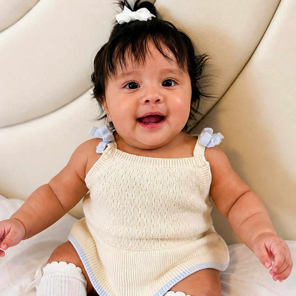Fiorella joined the competition — help win amazing prizes! baby, child, smiling, happy, sitting, knitted_dress, bow, hair, white_socks, indoors, cushioned_background, cute, portrait, infant, skin, face, arms, legs, expression, young