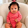 Fiorella is registered to the contest to win money with this photo: baby, infant, child, pink_outfit, bow, hair_tie, cute, armchair, indoor, portrait, smiling, chubby_legs, cozy, comfortable, curly_hair, skin, furniture, person, sitting, closeup
