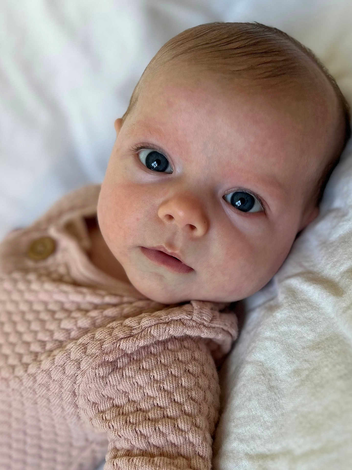 Sabrina is registered to the contest to win money with this photo: baby, infant, close_up, face, eyes, pink_clothing, knitwear, texture, soft, white_background, portrait, cute, young_child, child, newborn, skin, expression, lying_down, innocent, warm
