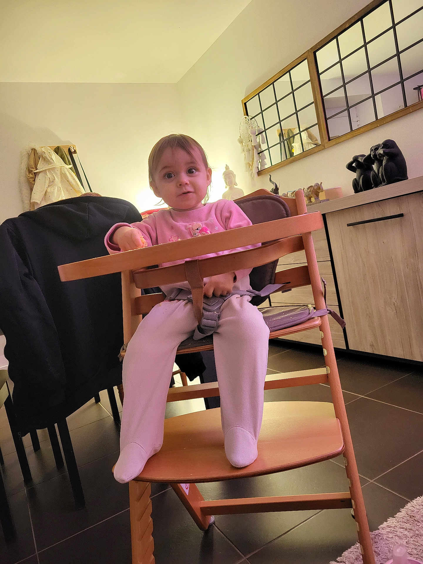 Lauëline participe au concours pour gagner de l'argent avec cette photo : child, toddler, highchair, baby, indoor, living_room, mirror, dresser, statue, toy, pink_clothing, socks, wooden_chair, tray, seatbelt, floor_tiles, coat, lamp, portrait, curiosity