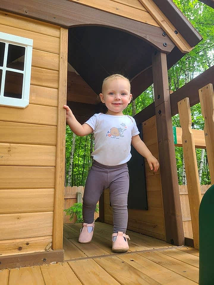 Camilla is registered to the contest to win money with this photo: baby_toddler_clothing, beauty, child, clothing, door, fun, grass, happy, house, joy, leisure, people_in_nature, person, plant, shorts, smile, standing, t_shirt, toddler, tree