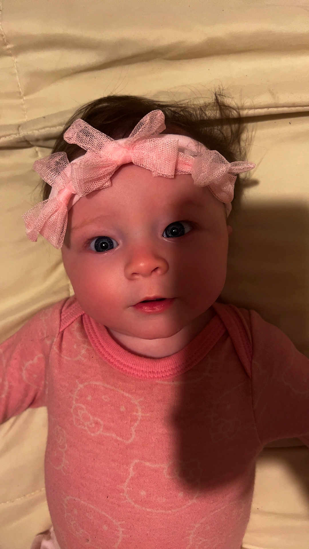 Madeline is registered to the contest to win money with this photo: baby, infant, pink, headband, bow, clothing, face, person, cute, portrait, onesie, hello_kitty, sleepwear, lying_down, indoors, child, small_child, baby_girl, expression, shadow
