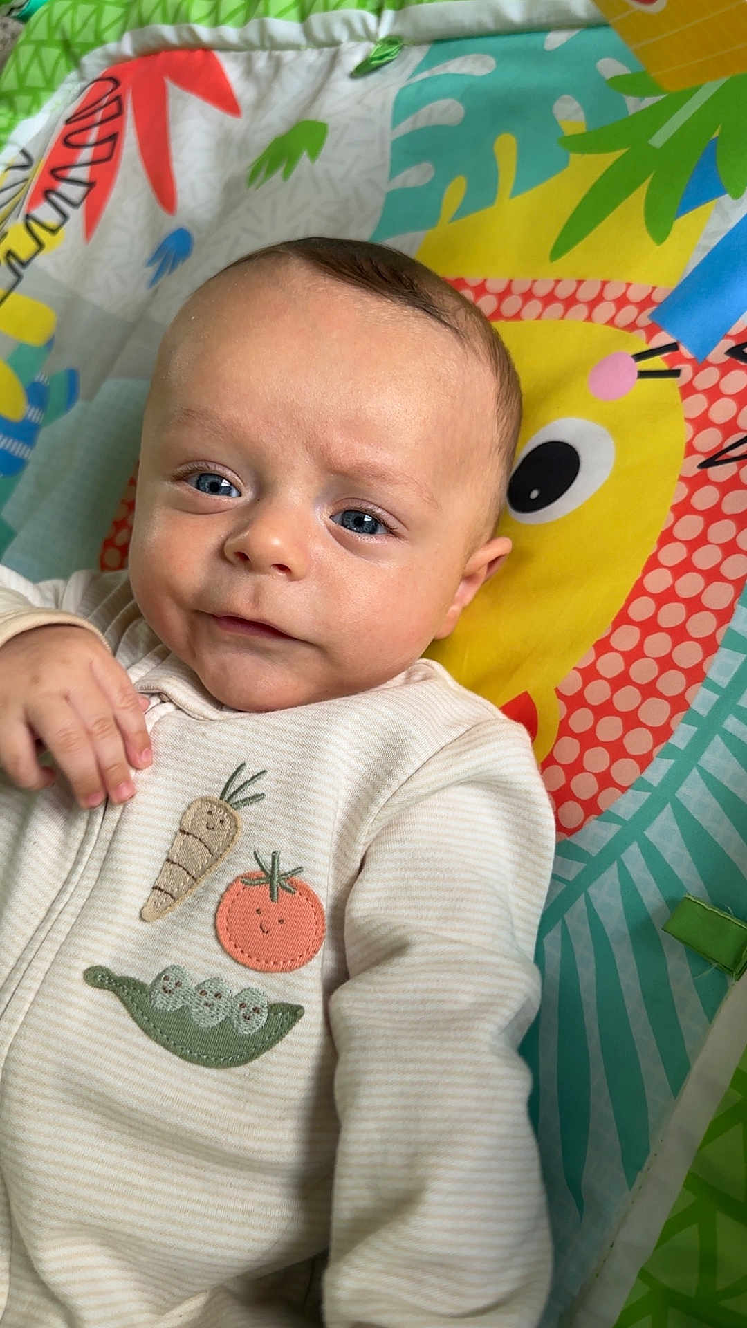 Chase joined the competition — help win amazing prizes! baby, infant, child, blue_eyes, face, hand, clothing, onesie, vegetable_patches, play_mat, colorful, yellow_character, cute, smiling, indoors, portrait, closeup, soft_lighting, expression, person