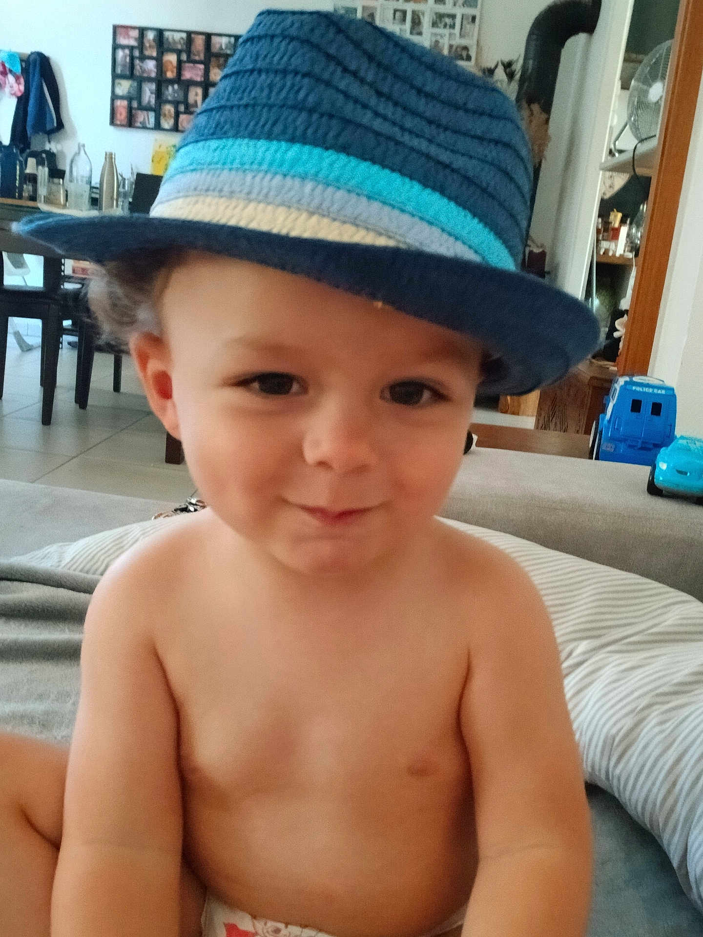 Elliott a rejoint le concours — aidez-le/la à gagner de superbes lots ! toddler, child, hat, fedora, blue, striped, smile, indoor, living_room, toy, diaper, cheeky, face, person, shirtless, curly_hair, home, furniture, couch, playful