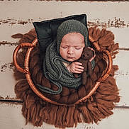 Maï a rejoint le concours — aidez-le/la à gagner de superbes lots ! baby, newborn, sleeping, basket, knitted_wrap, knitted_hat, teddy_bear, brown_blanket, cozy, infant, cute, portrait, soft_texture, resting, child, peaceful, wooden_floor, wrapped, hands, closeup