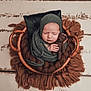 baby, newborn, sleeping, basket, knitted_wrap, knitted_hat, teddy_bear, brown_blanket, cozy, infant, cute, portrait, soft_texture, resting, child, peaceful, wooden_floor, wrapped, hands, closeup