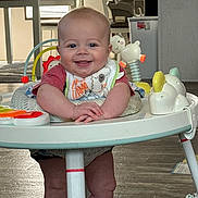 Dawson joined the competition — help win amazing prizes! baby, bib, chair, child, face, floor, furniture, hands, happy, home, indoor, infant, kitchen, legs, person, play, smiling, table, toy, walker