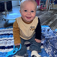 Dawson is registered to the contest to win money with this photo: baby, blanket, blue, child, clothing, face, floor, furniture, happy, home, indoor, jeans, person, playtime, quilt, smiling, socks, teething_toy, toys, white