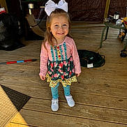 Gracelyn is registered to the contest to win money with this photo: casual_clothing, child, cord, cute, daylight, girl, happy, outdoor, person, pink_shirt, playful, portrait, smiling, standing, striped_leggings, table, tools, white_bow, white_shoes, wooden_floor