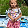 Gracelyn is registered to the contest to win money with this photo: child, girl, smiling, sitting, outdoor, grass, plant, leaf, water_bottle, box, clothing, skirt, tshirt, happy, person, portrait, daylight, nature, casual, cute