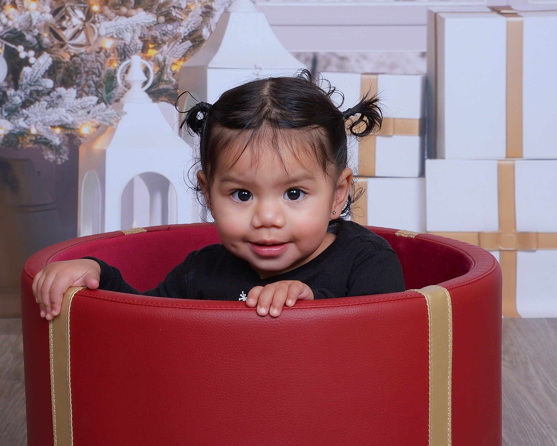 Zhurysadaii is registered to the contest to win money with this photo: toddler, child, girl, pigtails, red_seat, holiday, christmas, decorations, gifts, wrapped_presents, smiling, cute, indoor, portrait, floor, black_clothing, happy, face, hands, young_child