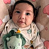 baby, infant, child, portrait, lying_down, plush_toy, dinosaur, stuffed_animal, blanket, bed, cozy, indoors, cute, wide_eyed, dark_hair, onesie, baby_clothing, pastel_colors, close_up, smiling