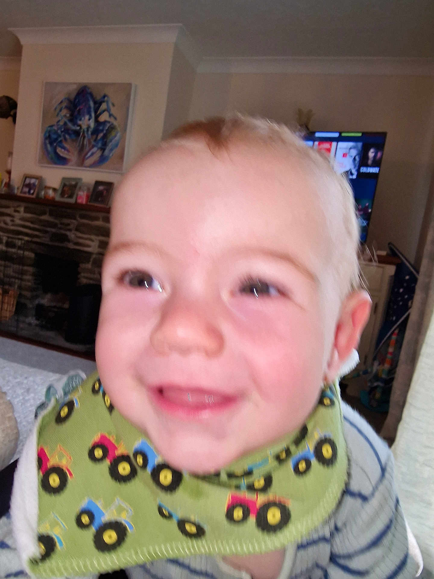 Bodhi joined the competition — help win amazing prizes! toddler, child, smile, face, bib, clothing, indoor, living_room, television, fireplace, stone, toy, happy, person, head, eyes, hair, cheeks, baby, home