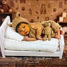 baby, newborn, knitted_hat, knitted_outfit, teddy_bear, mini_bed, pillow, blanket, sleeping, cute, infant, wooden_floor, plush_rug, toy_blocks, background, warm_lighting, portrait, child, cozy, soft_texture