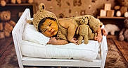 Omar is registered to the contest to win money with this photo: baby, newborn, knitted_clothing, bear_hat, miniature_bed, pillow, blanket, stuffed_toy, teddy_bear, fur_rug, wooden_floor, nursery, sleeping, infant, cute, portrait, child, cozy, soft_lighting, text_overlay