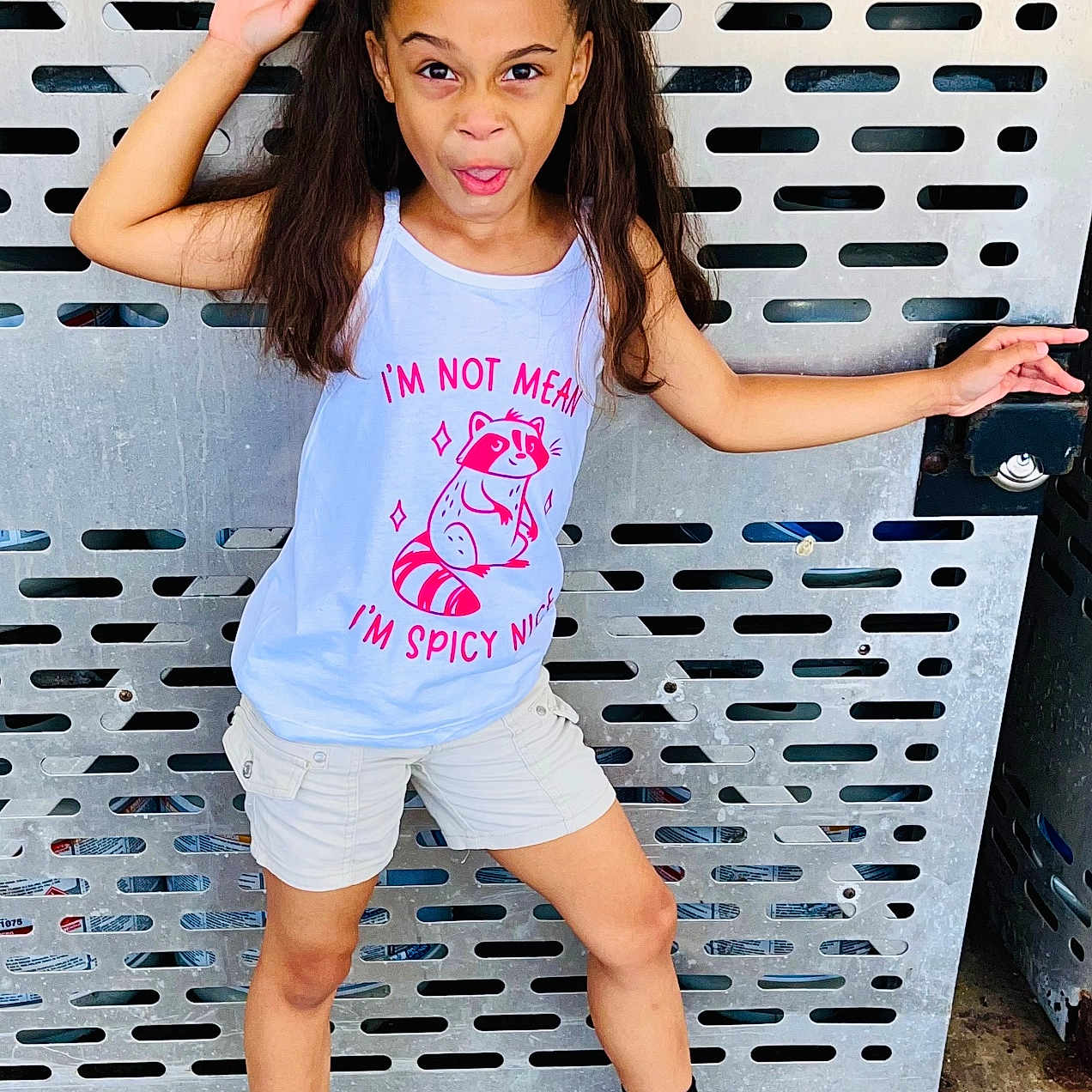 Charli is registered to the contest to win money with this photo: black_socks, casual_clothing, cheeky, child, concrete_floor, expression, fun, girl, graphic_tshirt, metal_background, outdoor, pink_bows, playful, pose, raccoon_graphic, shorts, standing, white_sneakers, white_tank_top, young
