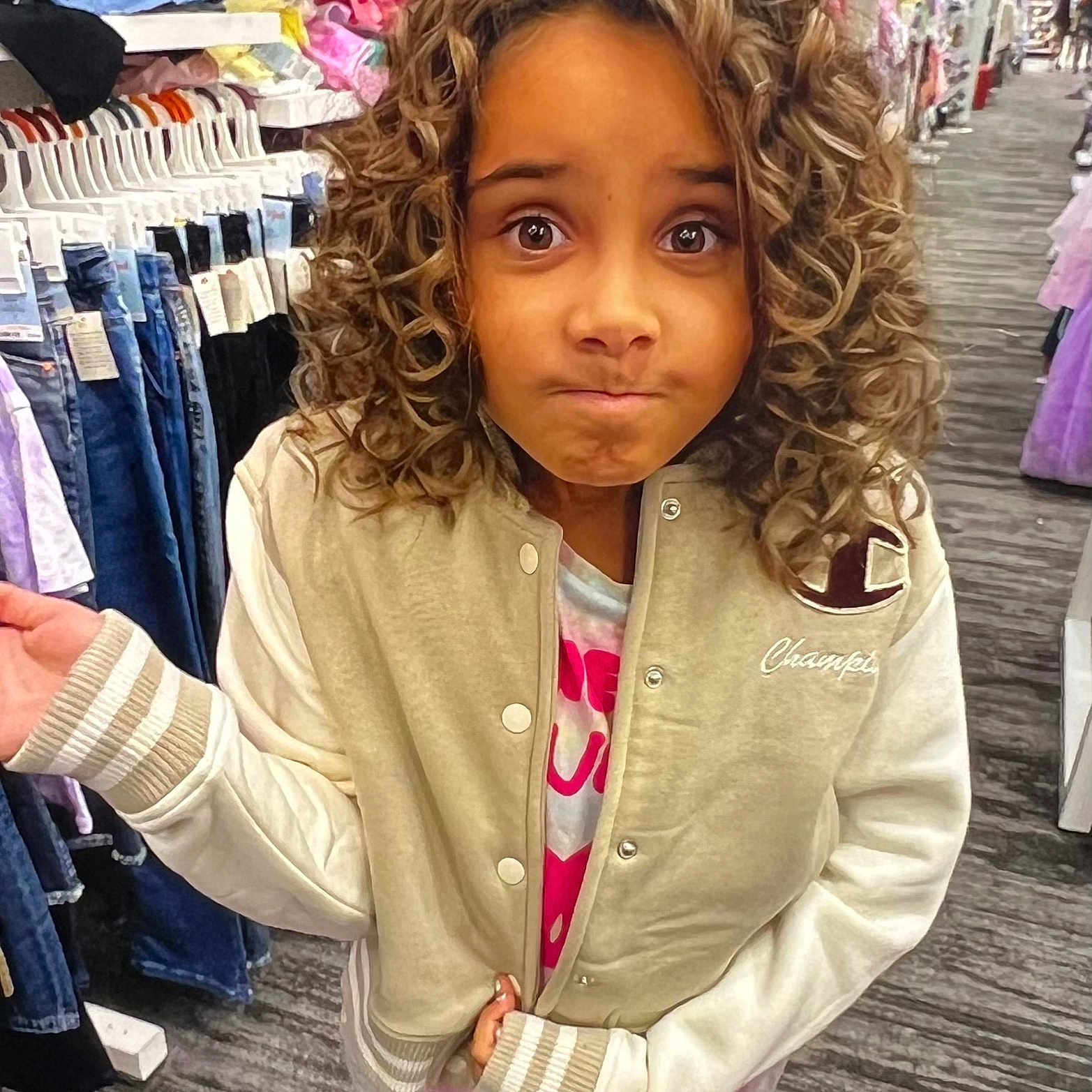 Kyah joined the competition — help win amazing prizes! apparel, casual_wear, child, clothing_store, curious_expression, curly_hair, floor, hand_gesture, indoor, jacket, jeans, long_sleeves, person, portrait, rack, retail, shopping, standing, store_aisle, young