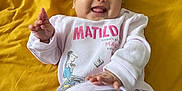 Matilda joined the competition — help win amazing prizes! baby, infant, smiling, happy, cute, child, lying_down, clothing, pajamas, yellow_blanket, hand, tongue_out, face, person, bed, comfort, playful, matilda, patterned_clothing, indoor
