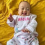 baby, infant, smiling, happy, cute, child, lying_down, clothing, pajamas, yellow_blanket, hand, tongue_out, face, person, bed, comfort, playful, matilda, patterned_clothing, indoor