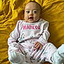 Matilda is registered to the contest to win money with this photo: baby, infant, child, pink_clothing, socks, lying_down, yellow_blanket, cute, happy, smiling, face, small_hands, onesie, cozy, playful, indoors, portrait, kicking_feet, young, person