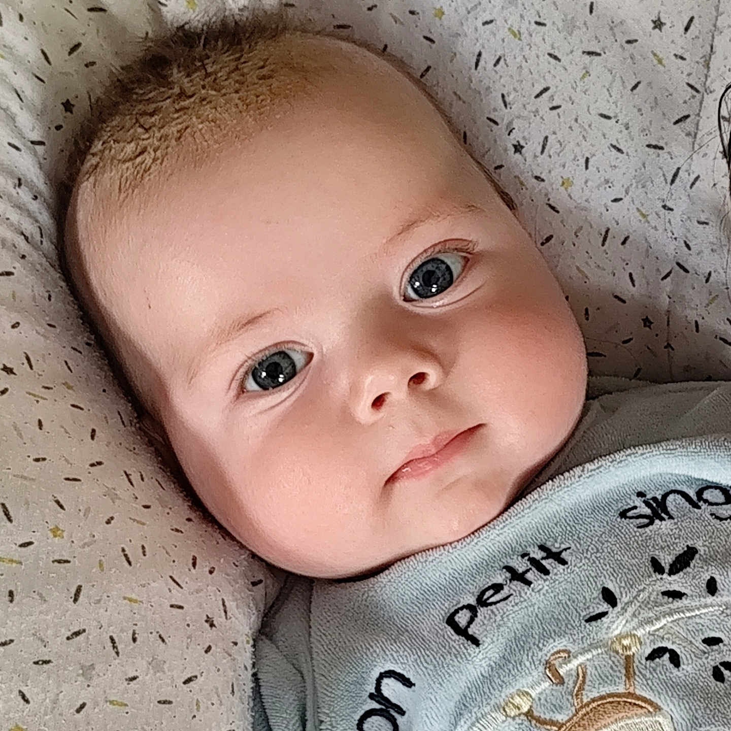 Kézio participe au concours pour gagner de l'argent avec cette photo : adorable, baby, blue_eyes, cheeks, child, closeup, clothing, cute, expression, face, indoors, infant, laying_down, monkey_design, pattern, pillow, portrait, soft_lighting, text_on_clothing, young