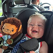 Max is registered to the contest to win money with this photo: baby, child, infant, smiling, happy, car, car_seat, passenger, driver, adult, plush_toy, monkey_toy, toy, vehicle, indoors, travel, portrait, seated, harness, family