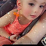 child, toddler, face, portrait, car_seat, seated, indoors, sparkles, filter, orange_clothing, pink_clothing, looking_at_camera, short_hair, earring, bracelet, vehicle, close_up, digital_effects, family, photograph